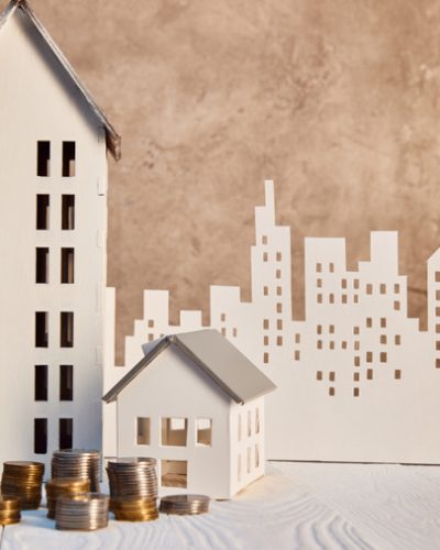 stock-photo-coins-houses-models-white-wooden-table-brown-textured-wall-paper stock-photo-coins-houses-models-white-wooden-table-brown-textured-wall-paper